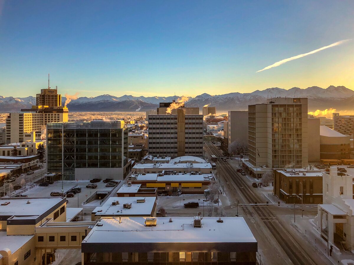 Downtown Anchorage at sunrise in winter, with snow on the rooftops and the Chugach Mountains behind