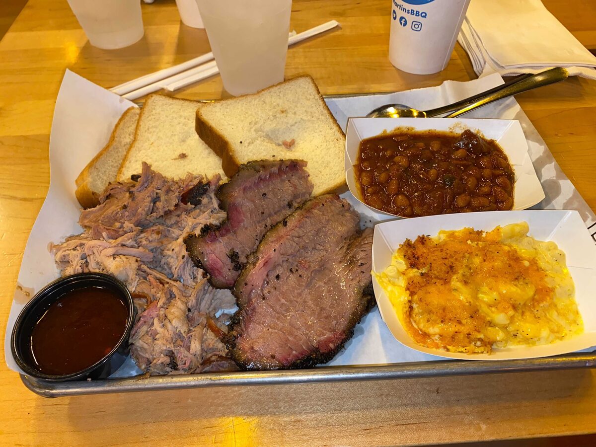 A barbecue tray with pulled pork, sliced brisket, baked beans, mac and cheese and white bread