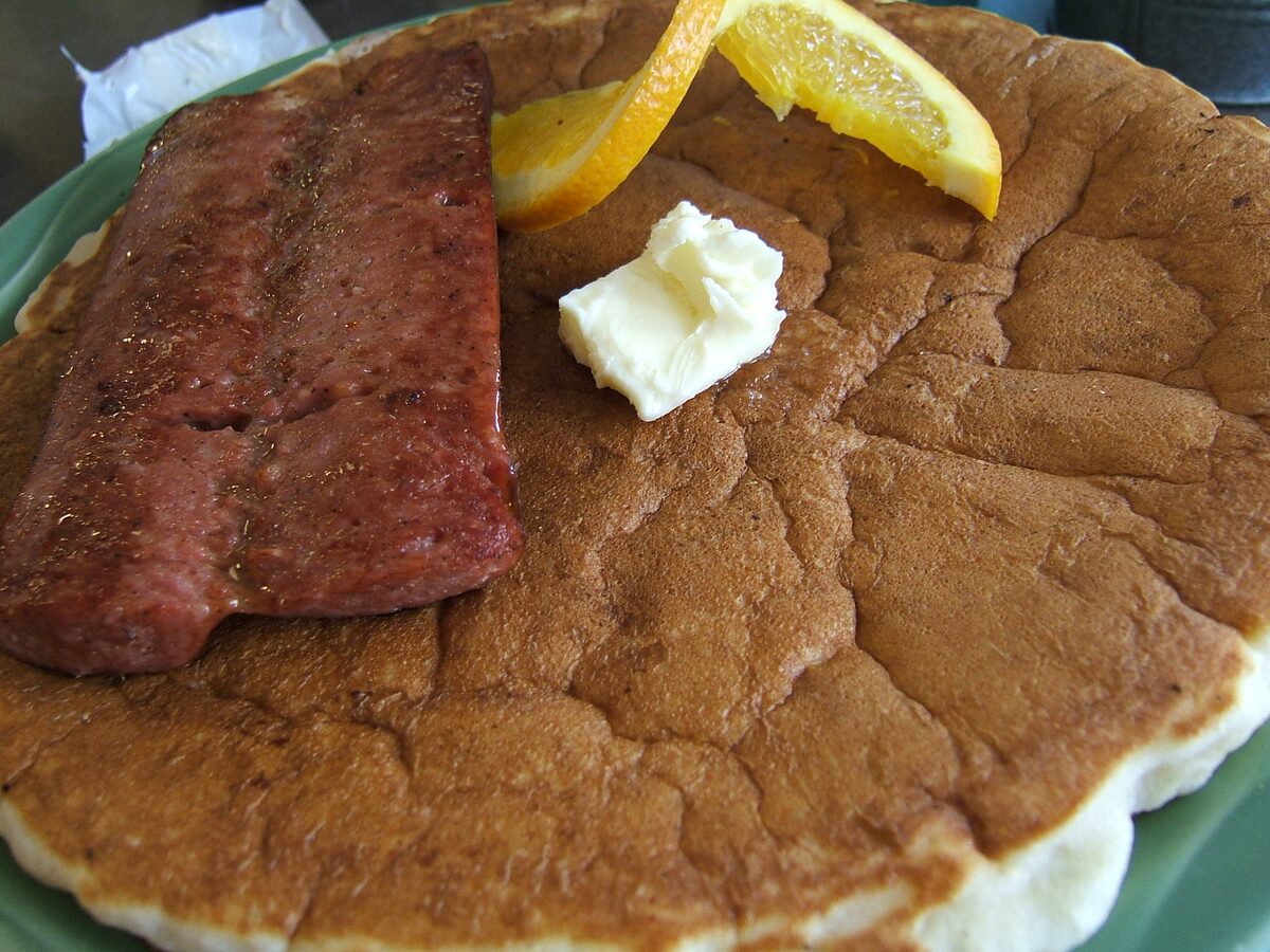 A thick pancake topped with a slab of reindeer sausage, a pat of butter and orange slices