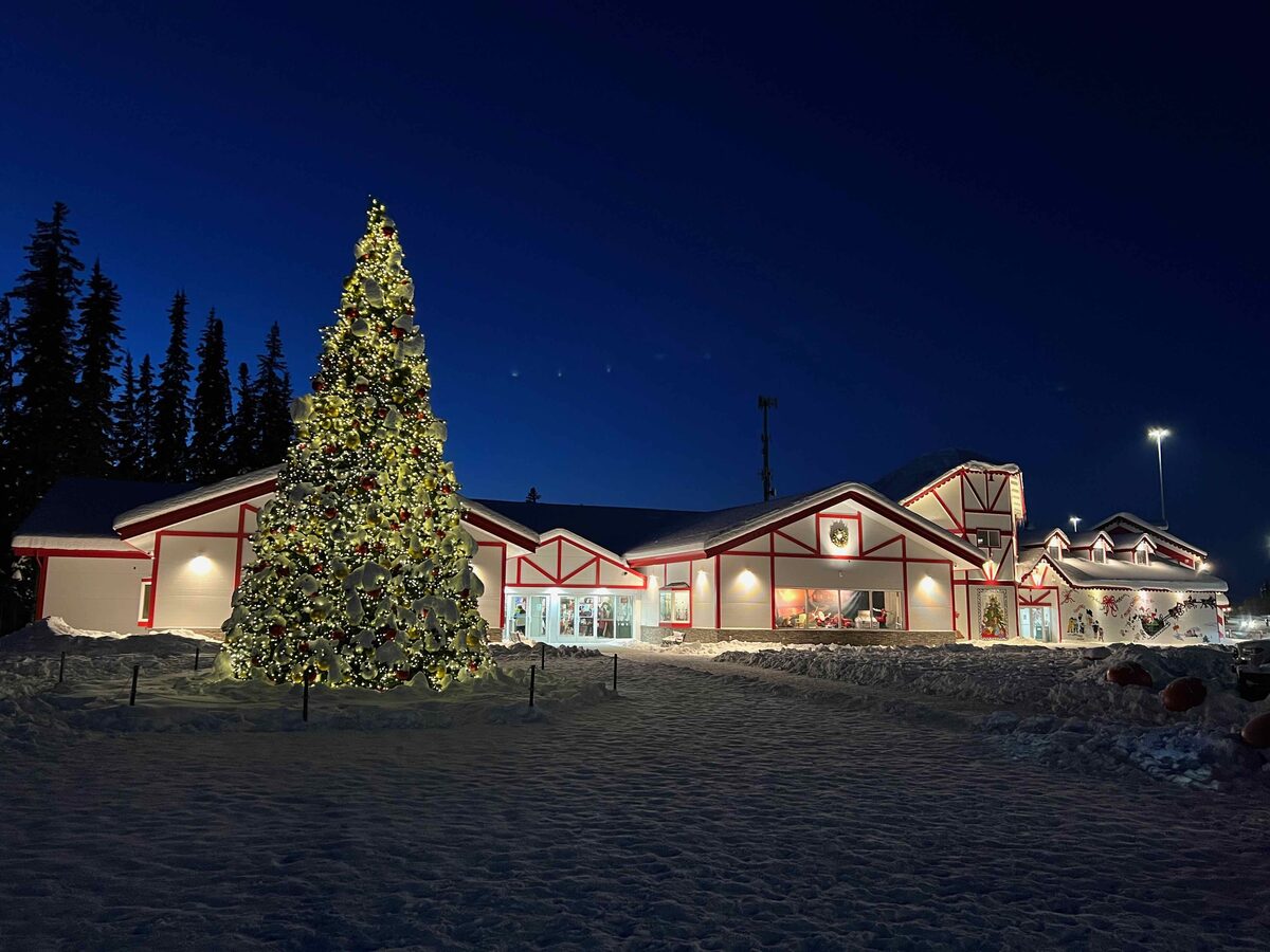 Santa Claus House in North Pole, Alaska, with a lit Christmas tree in front at dusk and snow on the ground