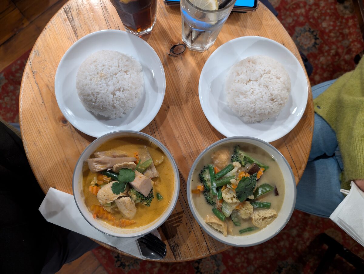 Two bowls of Thai curry with plates of steamed rice on a round wooden table