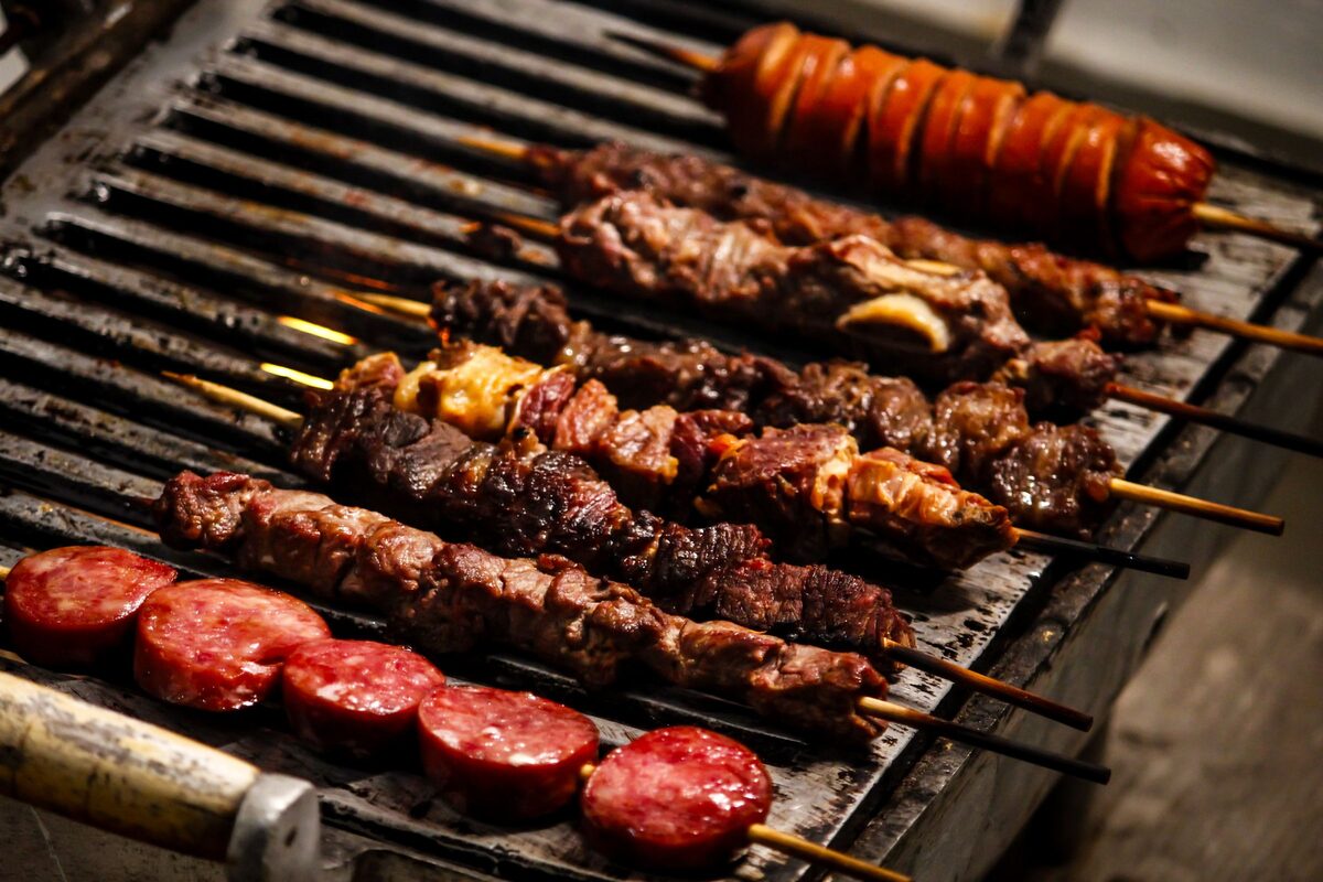 Beef, pork and sausage skewers lined up on a charcoal grill, the churrasco way