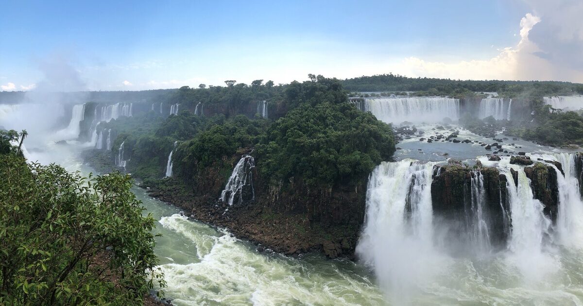 Iguazu Falls from the Brazilian side under a blue sky, a wide panorama of the cascades