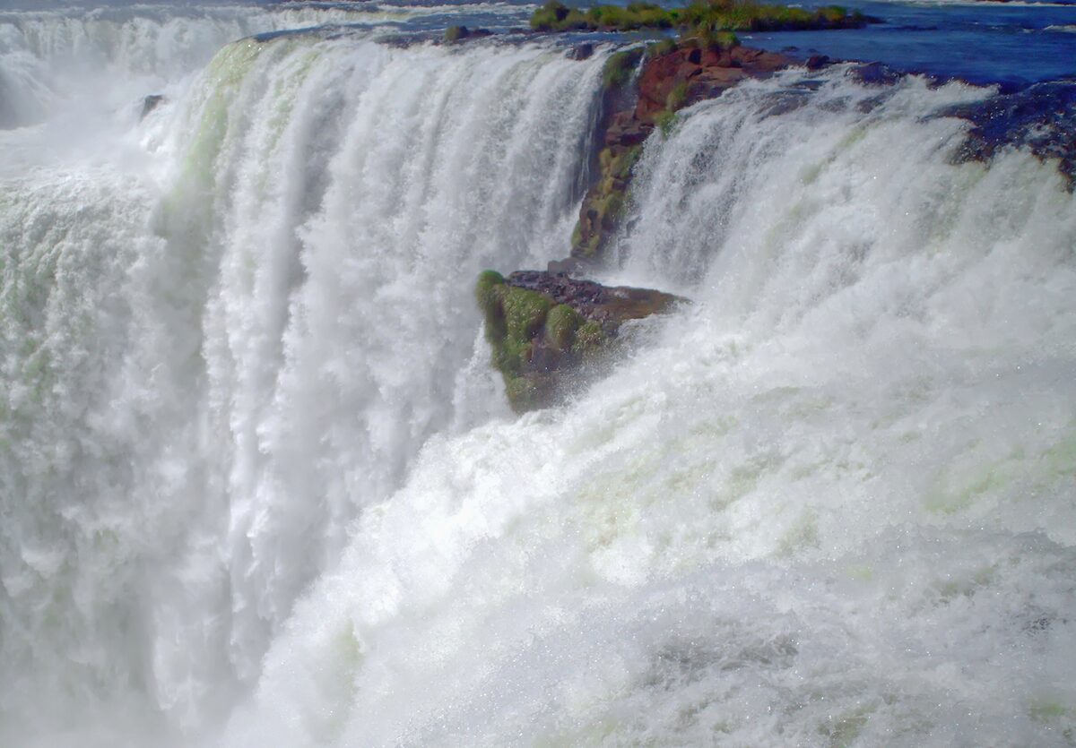 White water pours over the lip of the Devil's Throat, seen from the Argentine side, a mossy rock in the middle