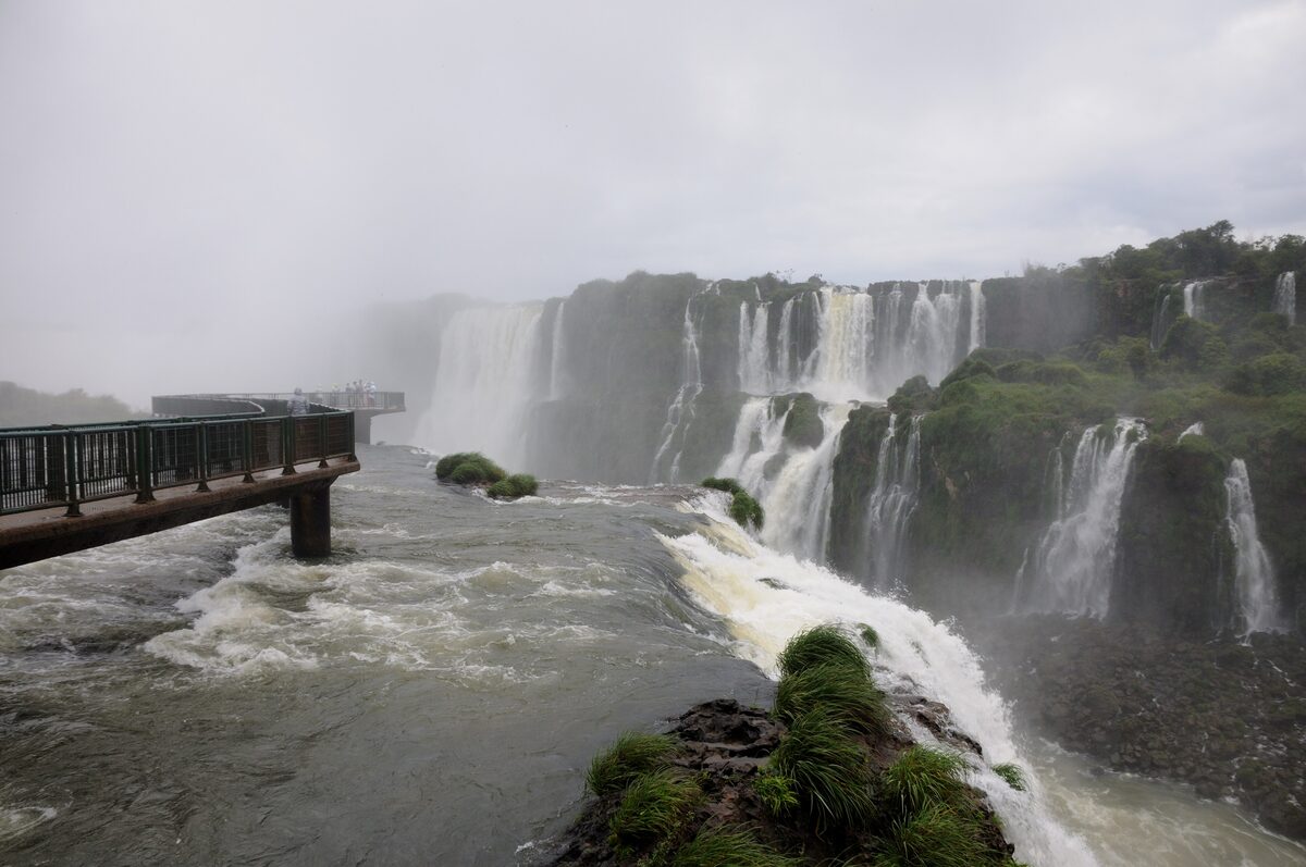The Brazilian Devil's Throat walkway juts out over the river toward the falls, with spray rising behind it