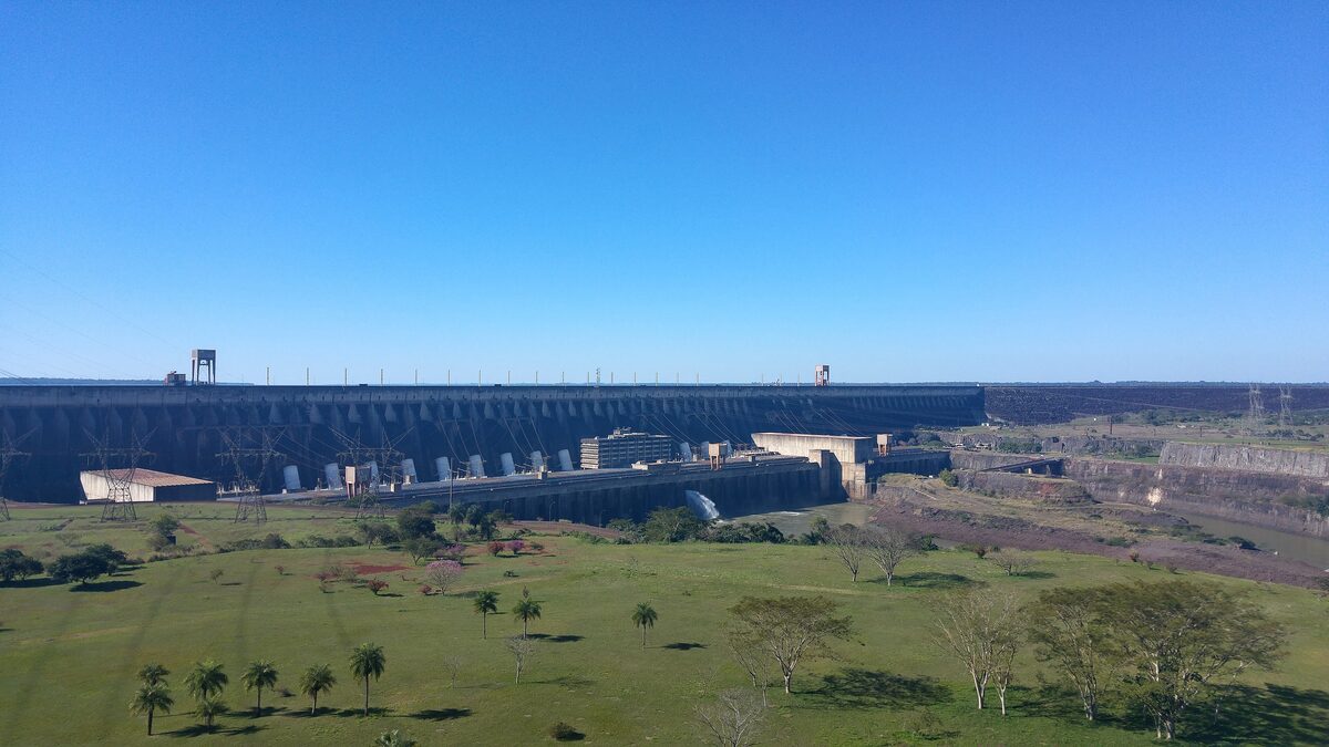 The long face of the Itaipu Dam stretching across the river, seen over open grass