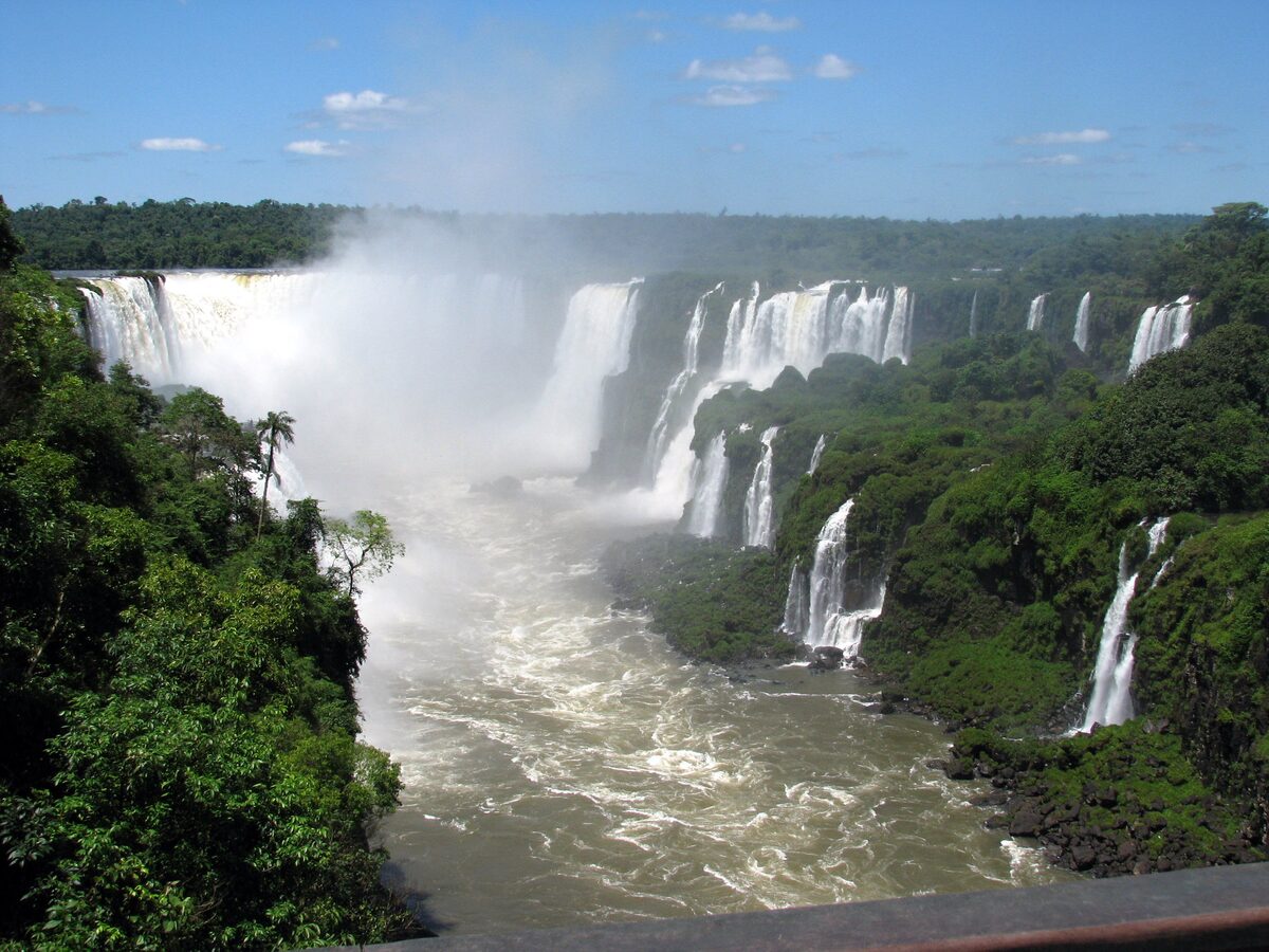The Iguazu Falls panorama from the Brazilian side, with a railing in the foreground and the Devil's Throat in the background