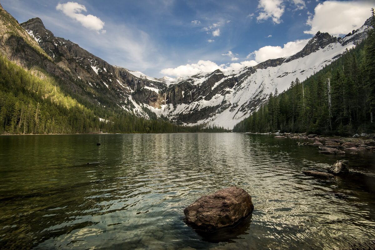 Avalanche Lake below steep snowfields and forested slopes