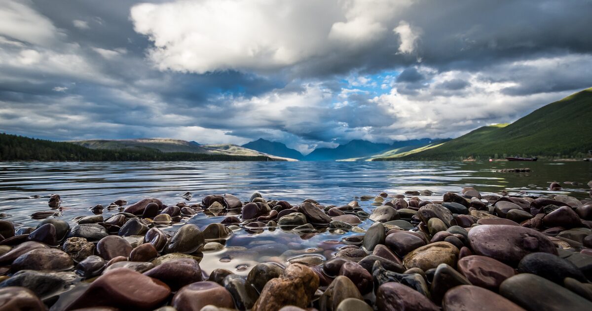 Colorful stones on the Lake McDonald shore beneath cloudy mountains