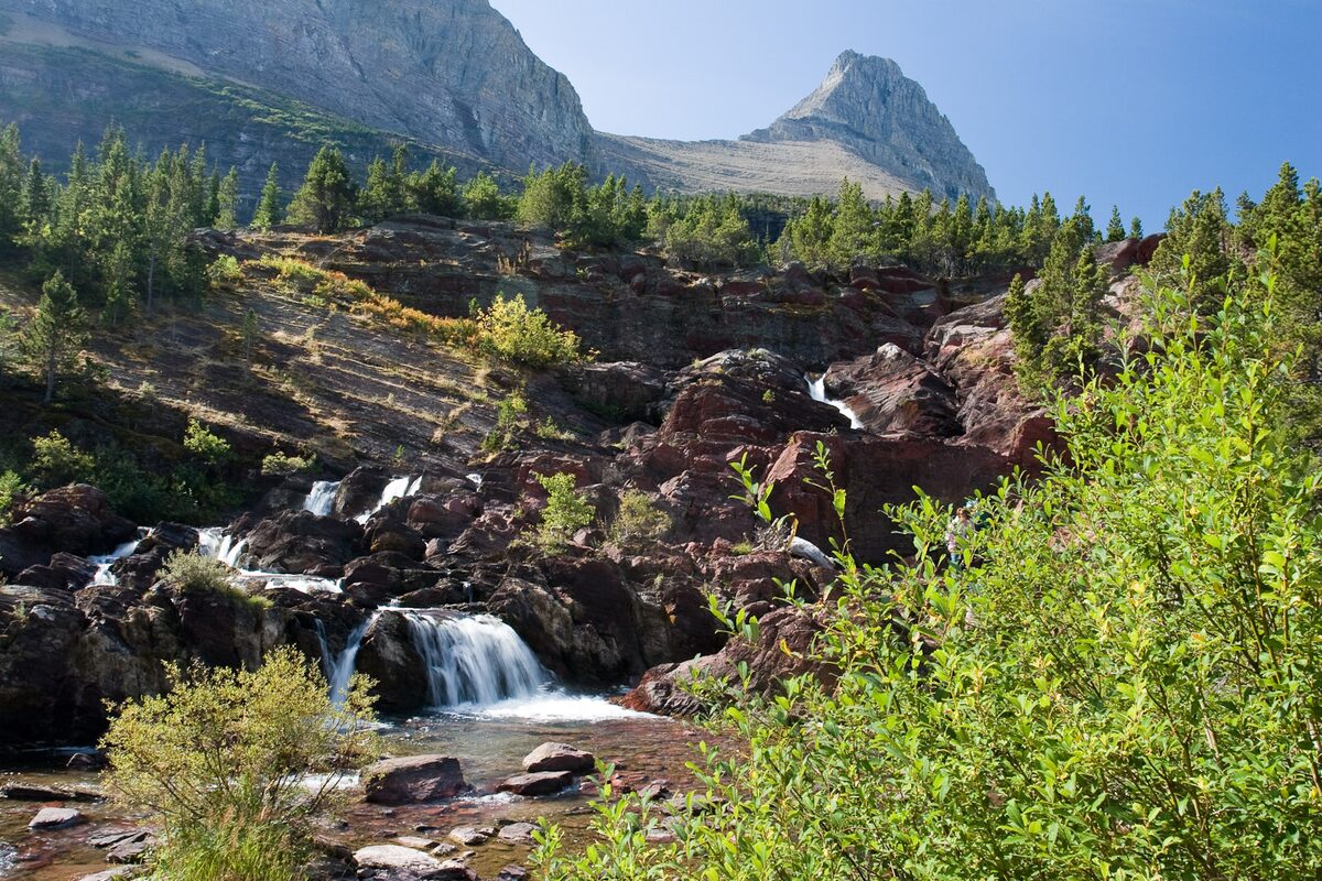 Redrock Falls cascading over red rocks below a rugged peak