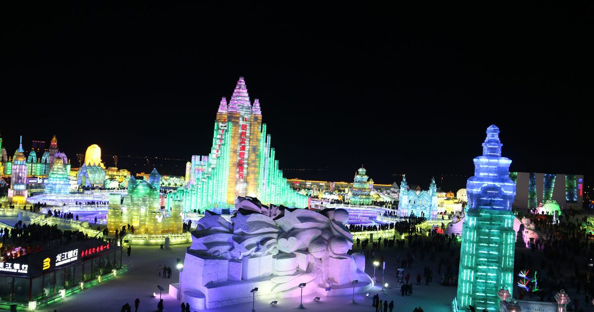 Illuminated ice buildings glowing in green, pink and blue against a dark sky at the Harbin Ice and Snow World