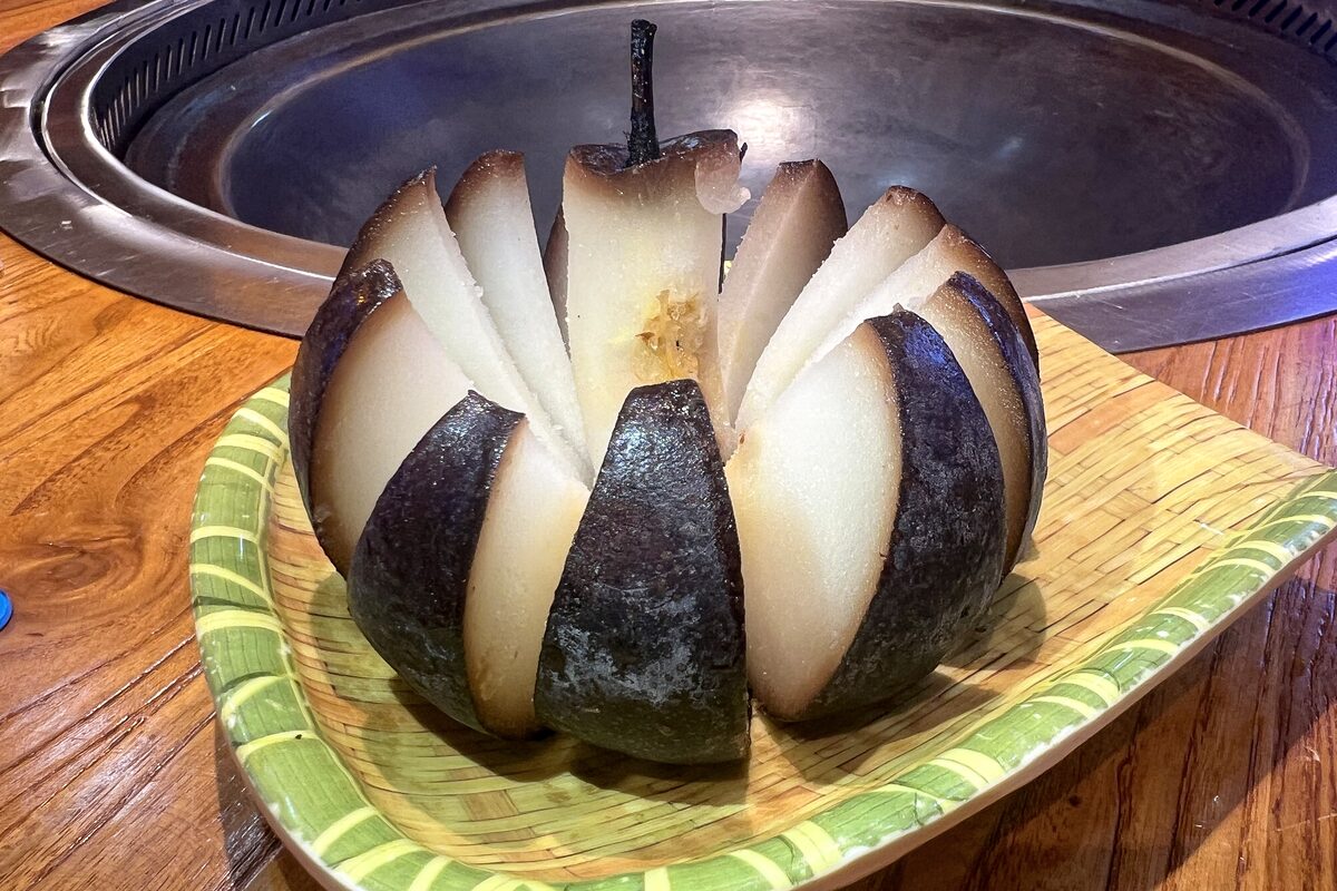A black frozen pear thawed and cut into wedges with pale flesh, on a woven dish at a Dongbei restaurant