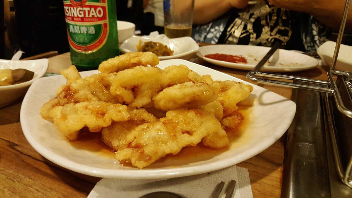 A plate of crisp battered pork slices in sweet and sour sauce on a restaurant table