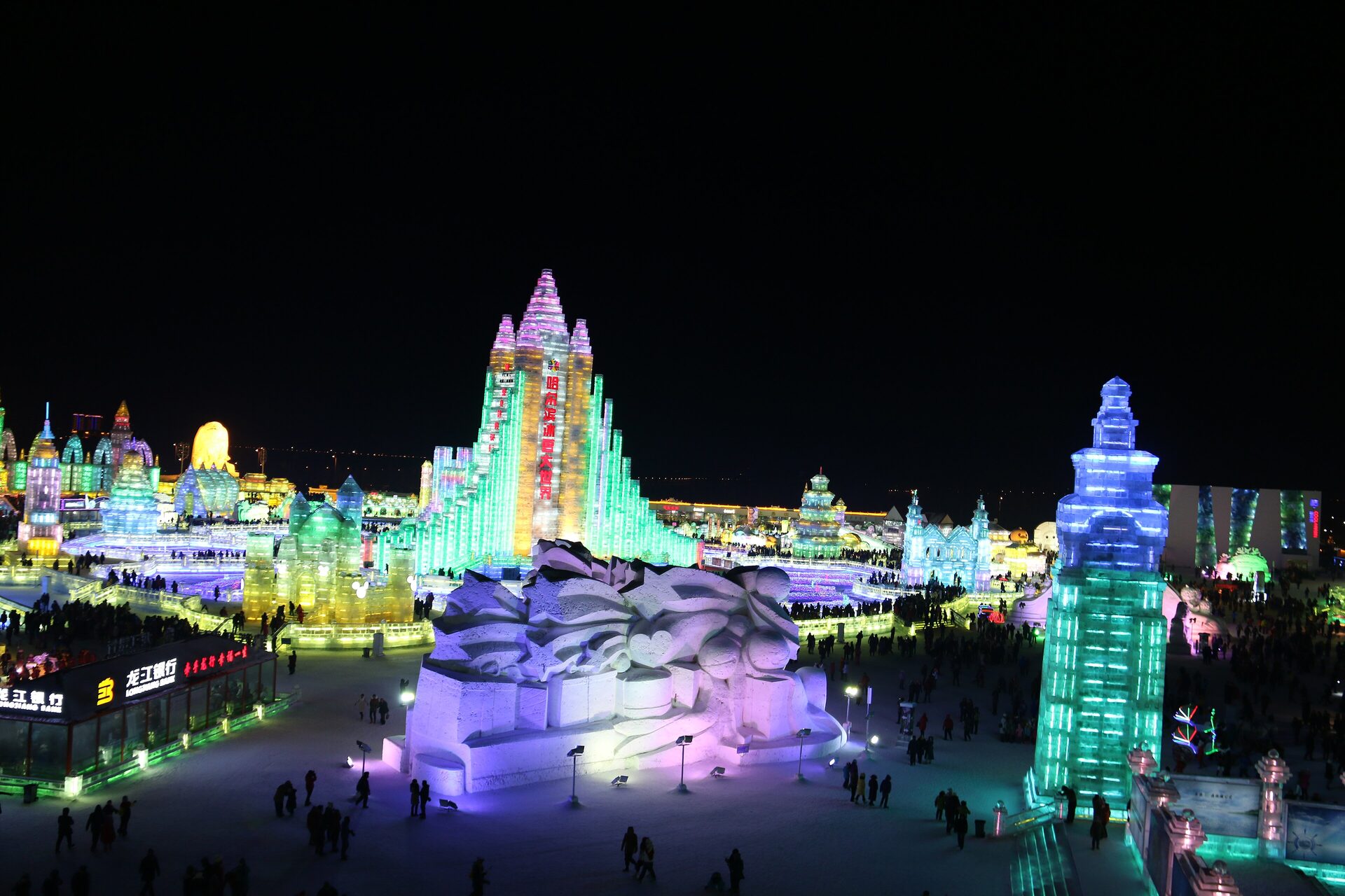 Illuminated ice buildings glowing in green, pink and blue against a dark sky at the Harbin Ice and Snow World