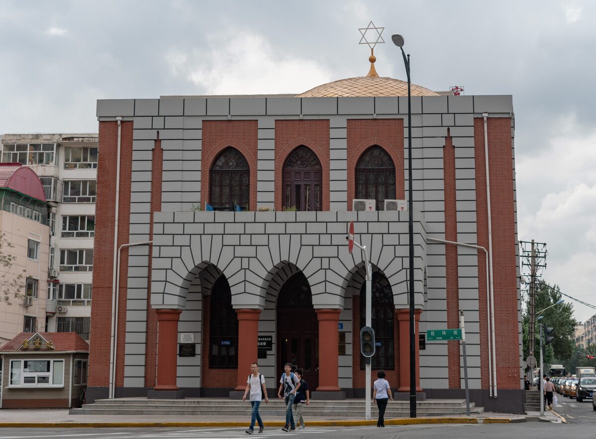 The red-brick and gray facade of the New Synagogue with three arched doors and a Star of David on top