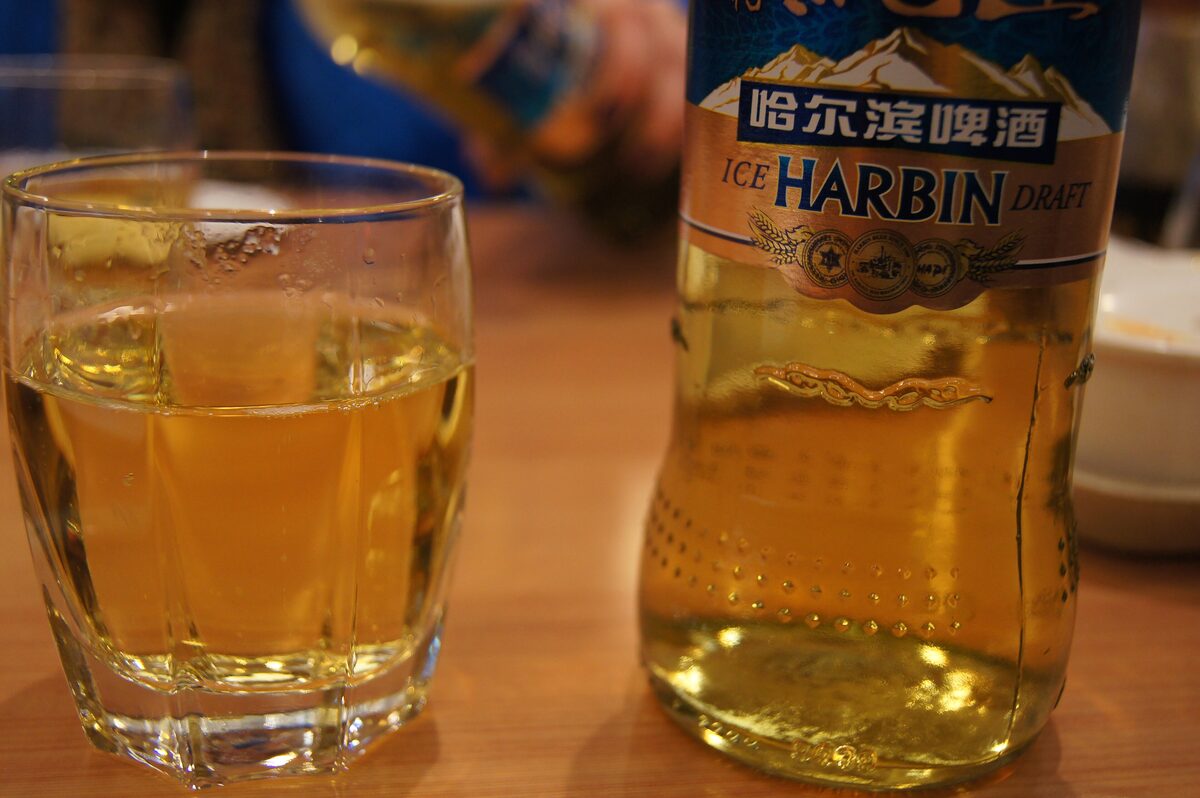 A glass of golden lager next to a Harbin Ice Draft beer bottle on a restaurant table