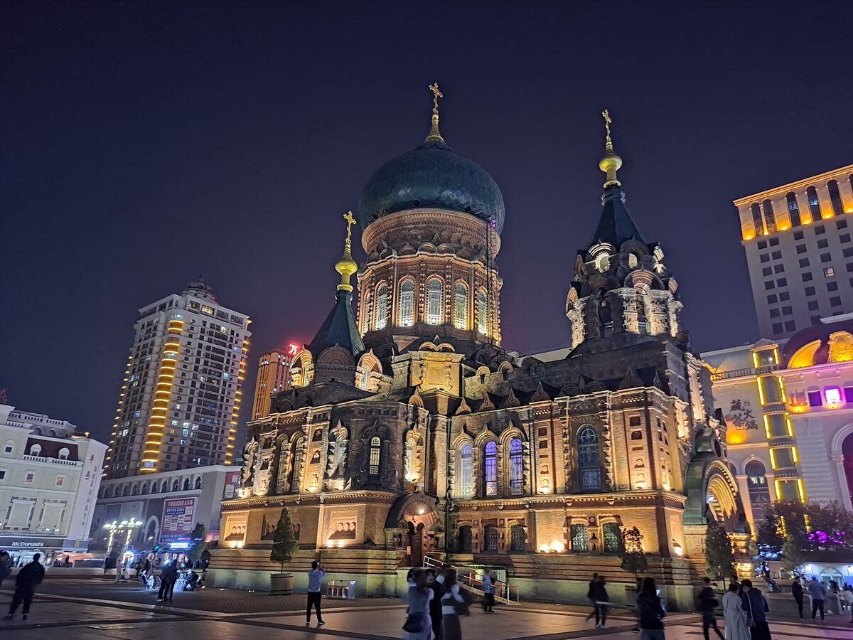 Saint Sophia Cathedral floodlit at night, its dark green dome and brick walls glowing above the square