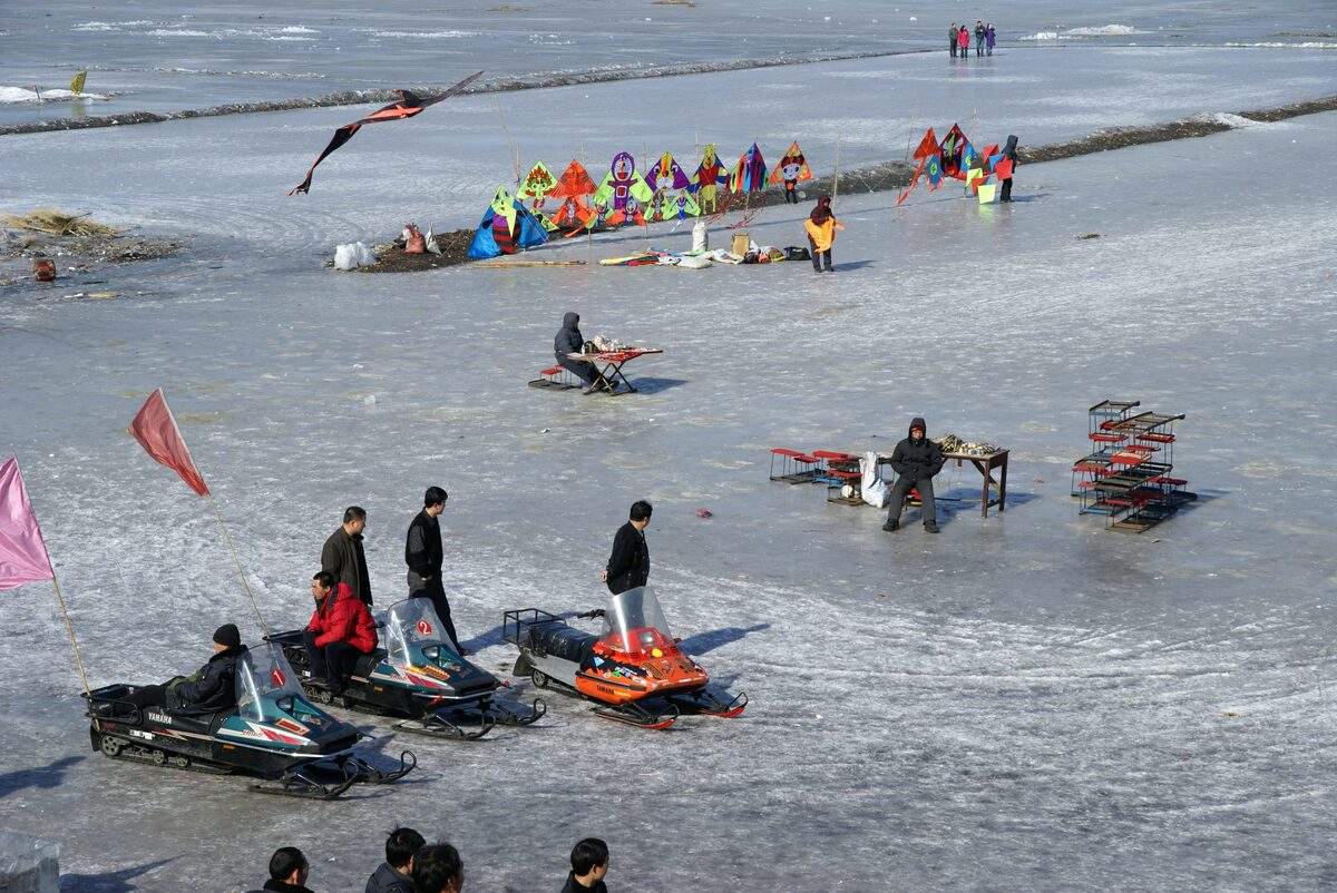People, snowmobiles and colorful kites on the frozen Songhua River
