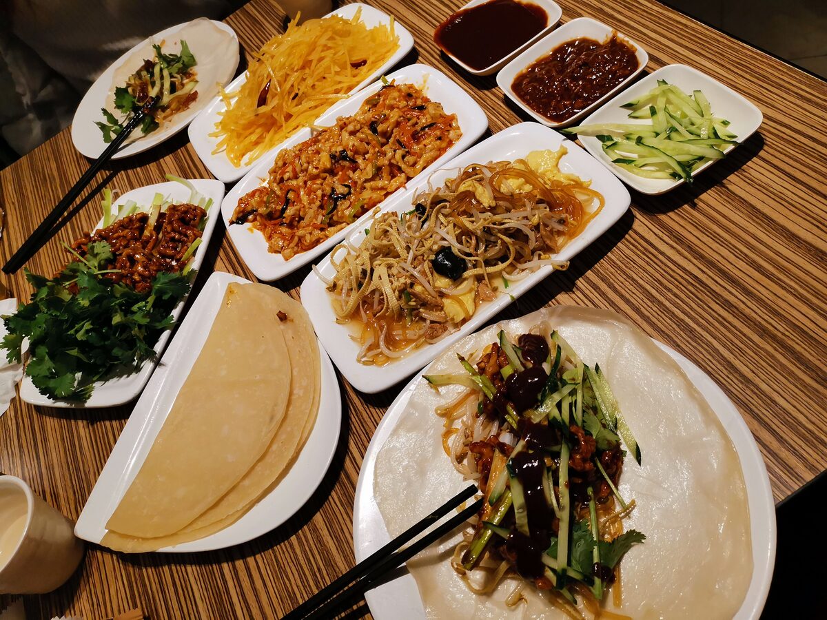 Plates of shredded potato, egg, vegetables and sauces laid out on a table with thin pancakes for wrapping