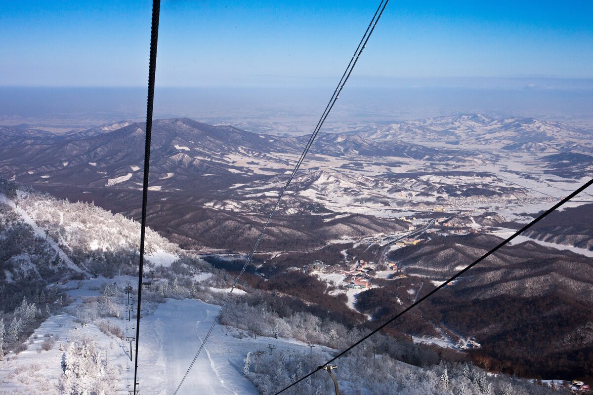 View from a ski lift over snowy forested mountains and a ski run at Yabuli