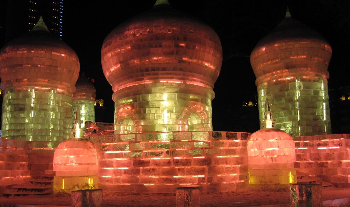 An ice castle with onion-shaped domes lit orange and yellow from inside at night in Zhaolin Park