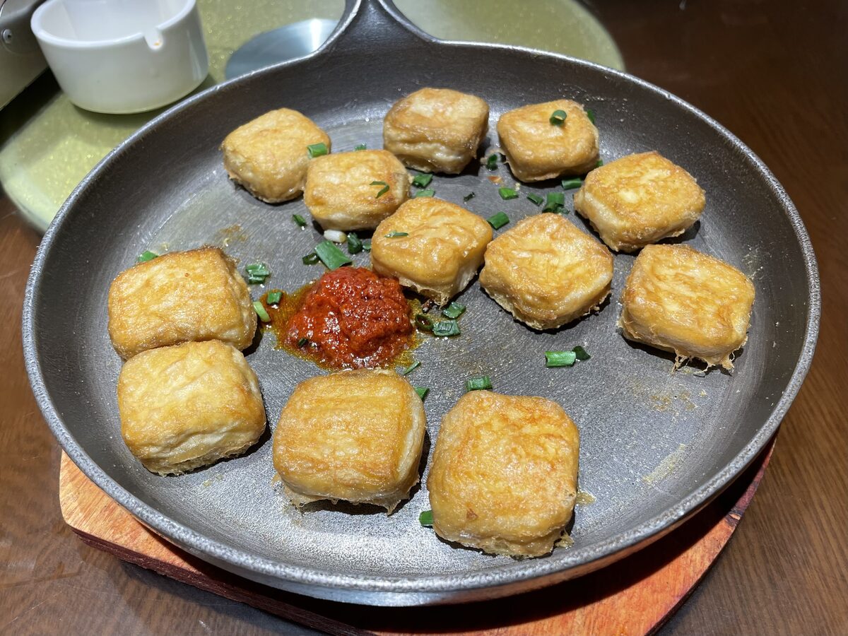 Pan-fried golden tofu cubes in an iron skillet with a spoonful of chili sauce and chives