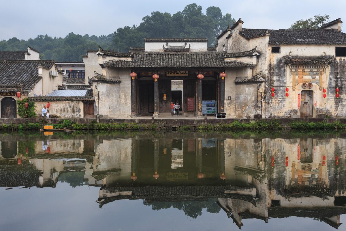 Old Huizhou houses with white walls and dark roofs reflected in the still water of Hongcun's pond
