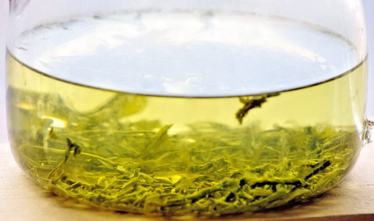Green tea leaves steeping in a glass pot of pale yellow-green tea
