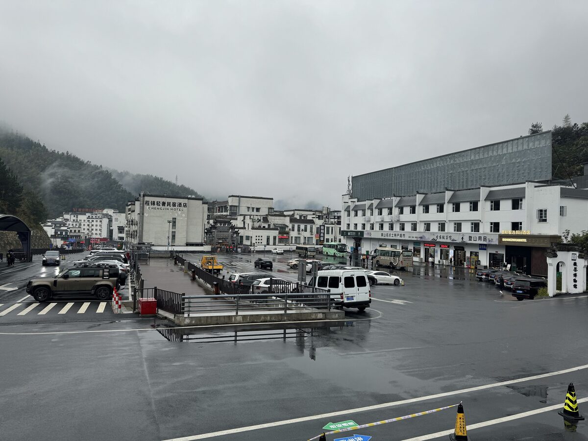 The Tangkou transfer center on a rainy day, with shuttle buses and cars in the car park and forested hills behind