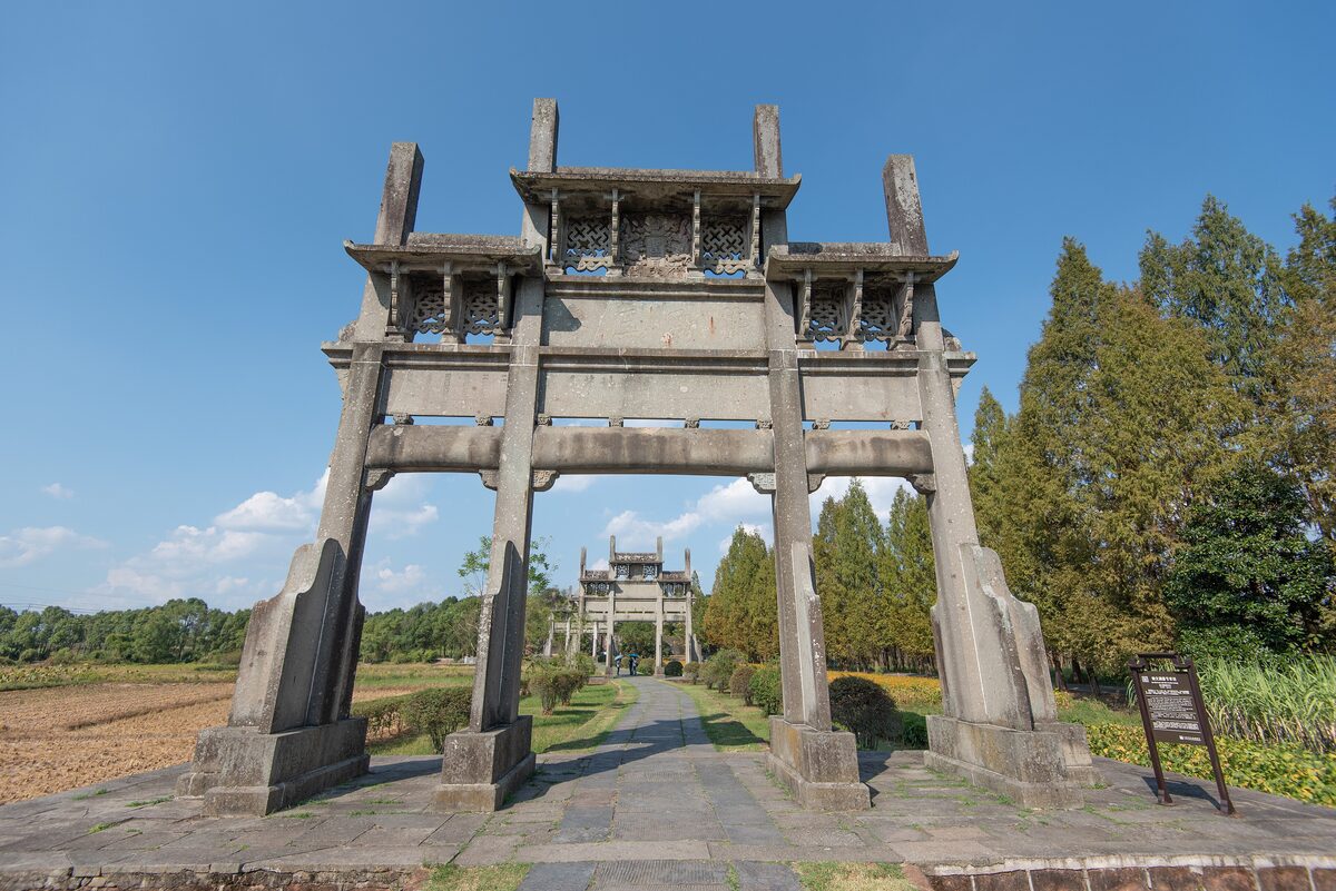 A stone memorial archway at Tangyue with more archways receding along a path between fields