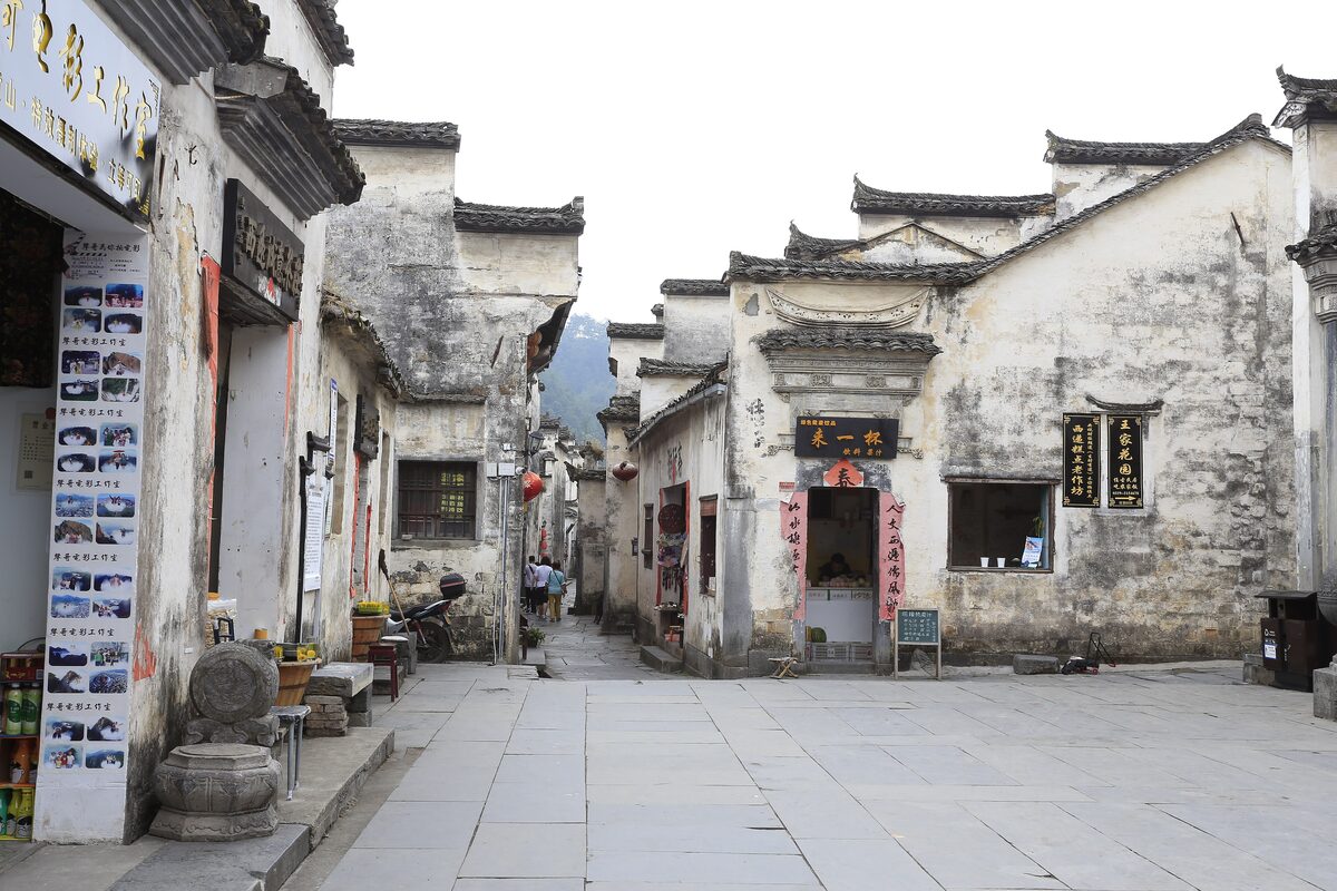 A paved lane in Xidi between weathered white Huizhou houses with dark tiled eaves