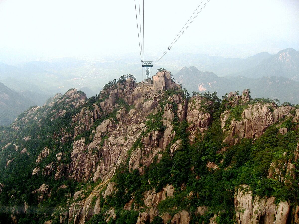 View from the Yungu cable car cabin of cables running above a granite ridge covered in pines