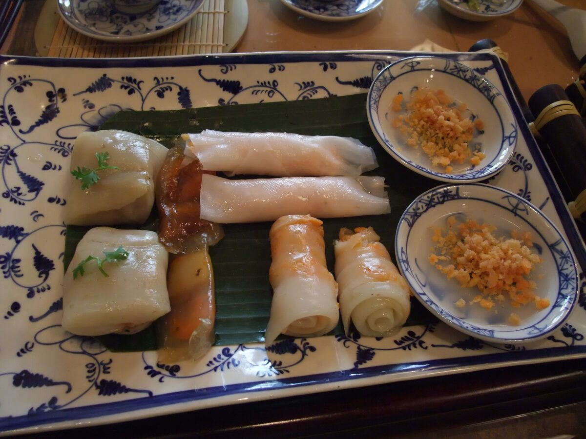 Steamed rice-flour banh nam and rolled loc on a banana leaf, with two dishes of crisp shrimp crumbs