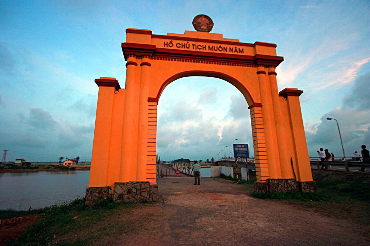 An orange memorial arch at the end of the Hien Luong Bridge over the Ben Hai River at dusk