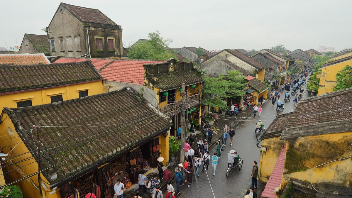 Crowds and motorbikes on a narrow street of yellow and ochre merchant houses in Hoi An