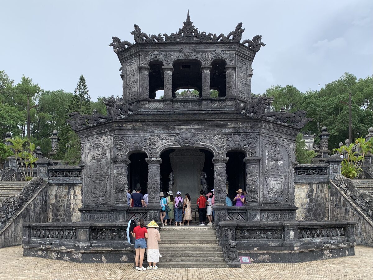 The ornate grey stone pavilion of Khai Dinh Tomb with visitors on its stairs