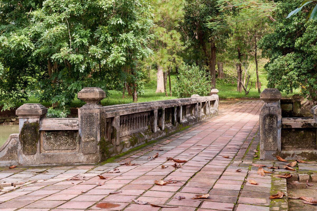 A stone-railed bridge over a paved path through trees at the Minh Mang Tomb