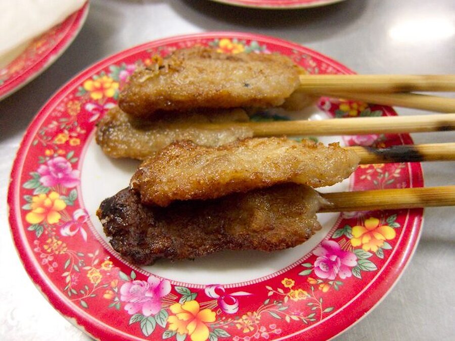 Four grilled minced-pork nem lui skewers on a red floral plate