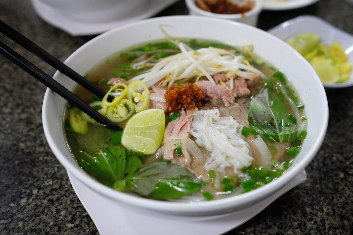 A bowl of beef pho with lime, herbs and chili and chopsticks resting in it