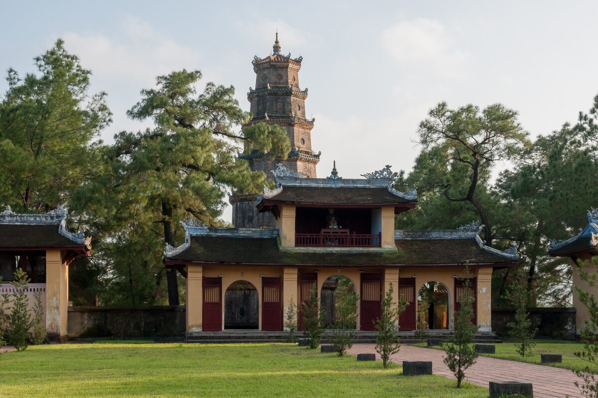 The gate pavilions of Thien Mu Pagoda on a lawn among pines, with the Phuoc Duyen Tower rising behind