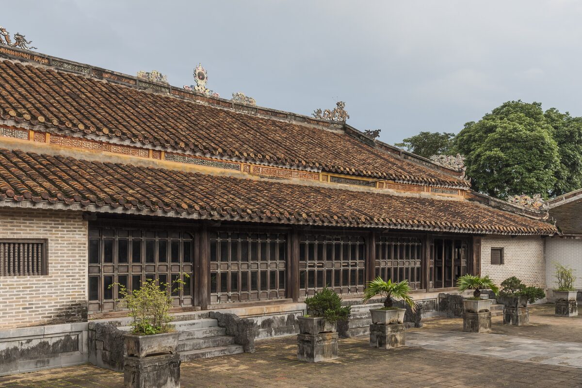 The long tiled palace building with brick walls and potted plants on its terrace at the Tomb of Tu Duc