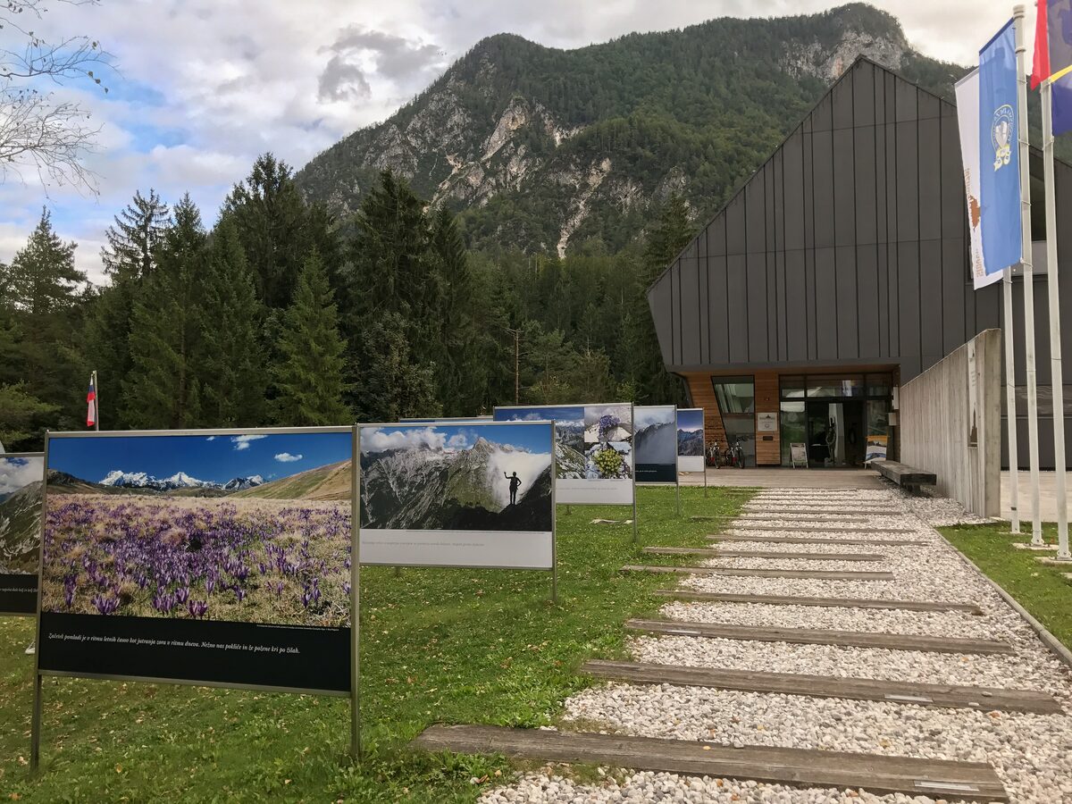 The Slovenian Alpine Museum in Mojstrana, a dark modern building with flag poles and a stone path across the lawn