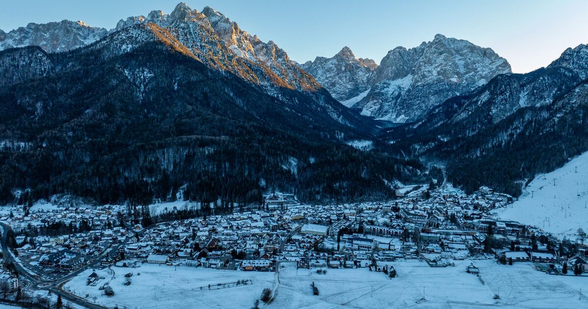 Aerial view of Kranjska Gora under snow on a clear winter day, with the village in the valley and the Julian Alps rising behind it