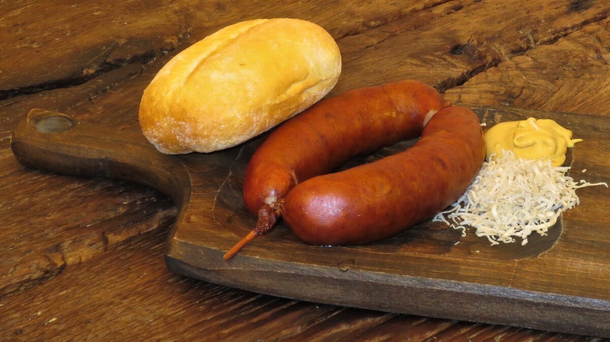 Carniolian sausages on a wooden board with a bread roll, mustard and grated horseradish