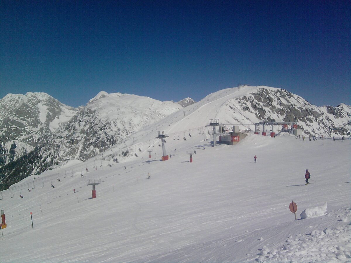 Snowy ski pistes and lift towers on Krvavec under a blue sky, with a skier on the slope