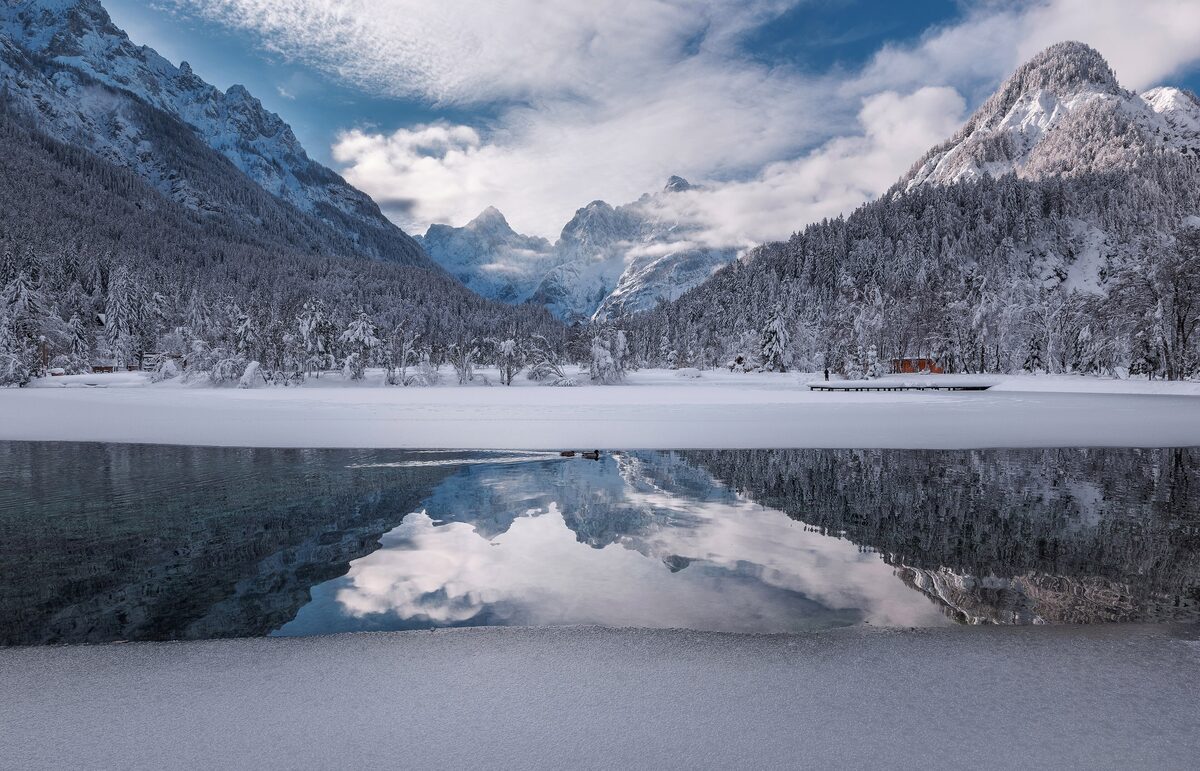 Lake Jasna on a winter day, with snow on the shore and the snowy mountains reflected in the dark water