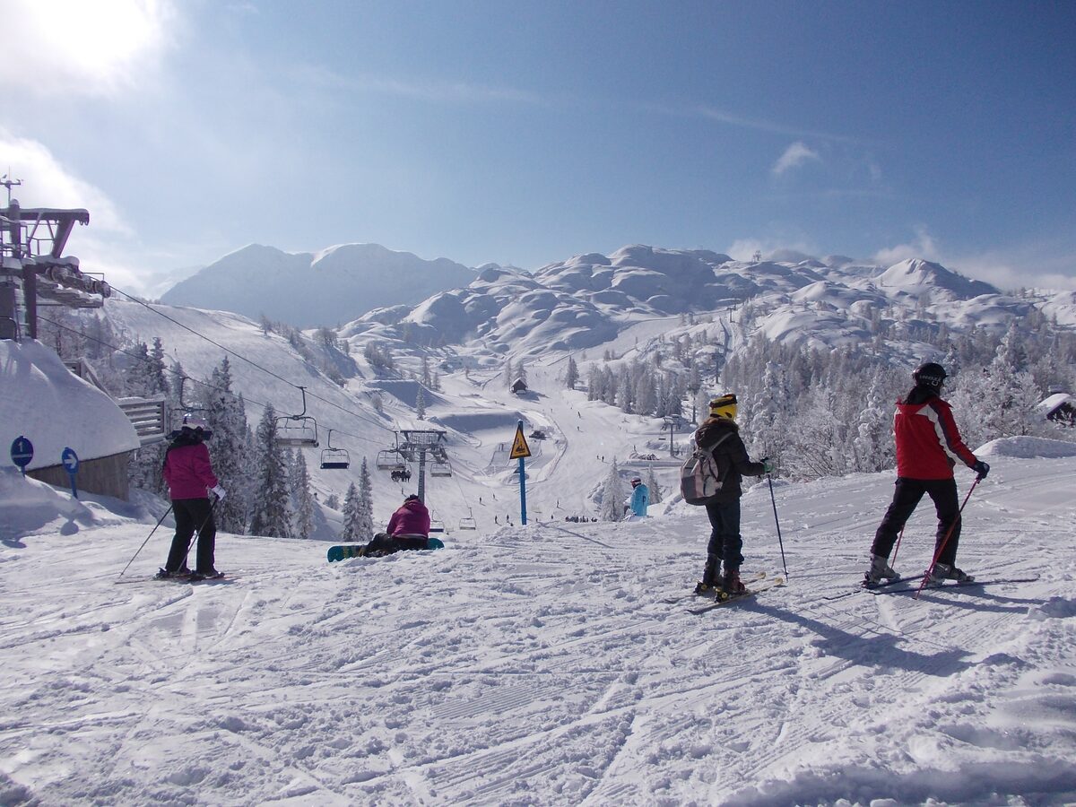 Four skiers on a sunny groomed piste at Vogel with a chairlift and snow-covered limestone mountains behind them