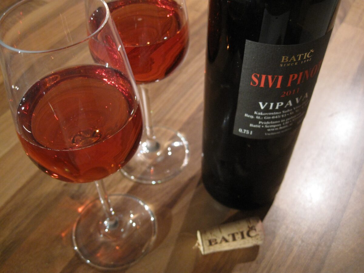 A bottle of Batič Sivi pinot from Vipava beside two glasses of pale orange wine