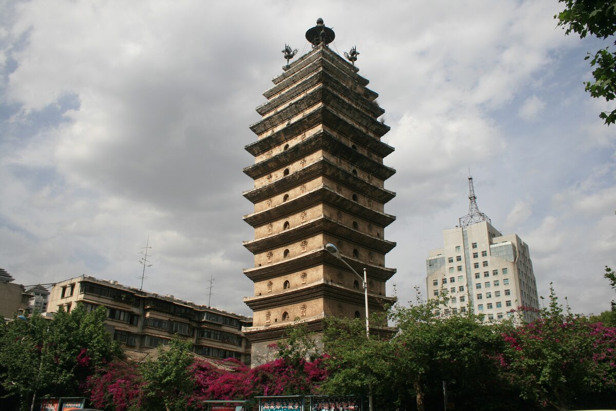 The tiered Eastern Pagoda rising above trees and flowering bushes, with city buildings beside it