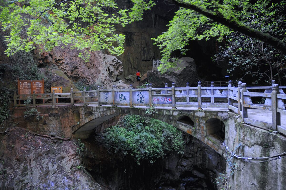 A stone bridge with a railing over a dark gorge in the Jiuxiang caves area